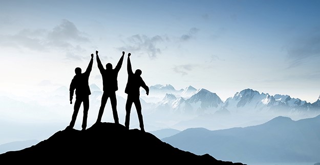 Three people atop a mountain cheering for victory