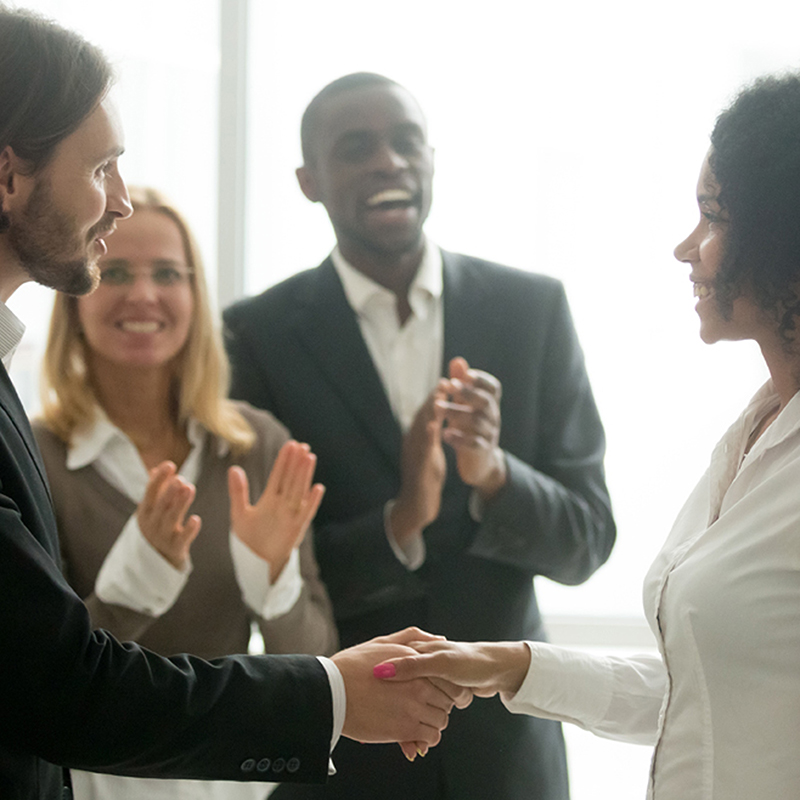 Grateful boss handshaking promoting african businesswoman congratulating with career achievement while colleagues applauding cheering successful worker