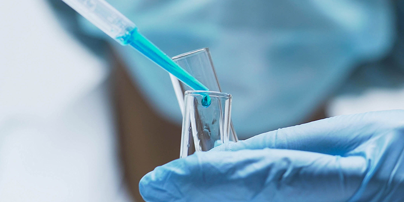 Female chemist adds drops of blue substance into test tubes, lab research