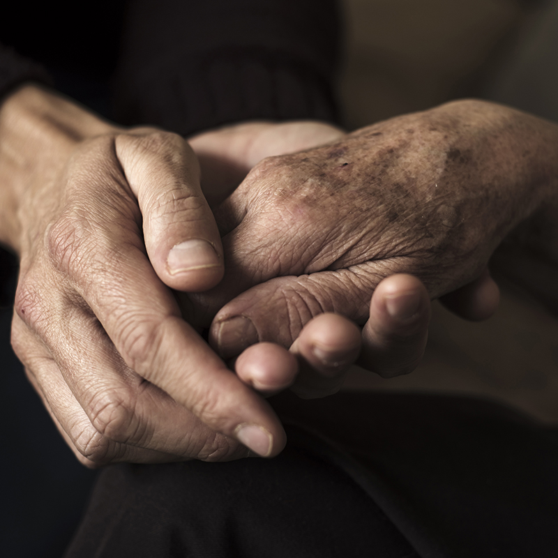 closeup of a young caucasian man holding the hand of an old caucasian woman with affection