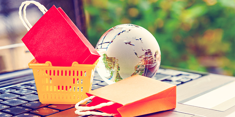 Shopping bags, shopping basket, and a globe sitting on a laptop keyboard
