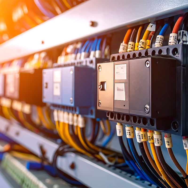 Close-up view of a professional electrical panel with labeled wires in bright colors, showcasing switches and circuit breakers.