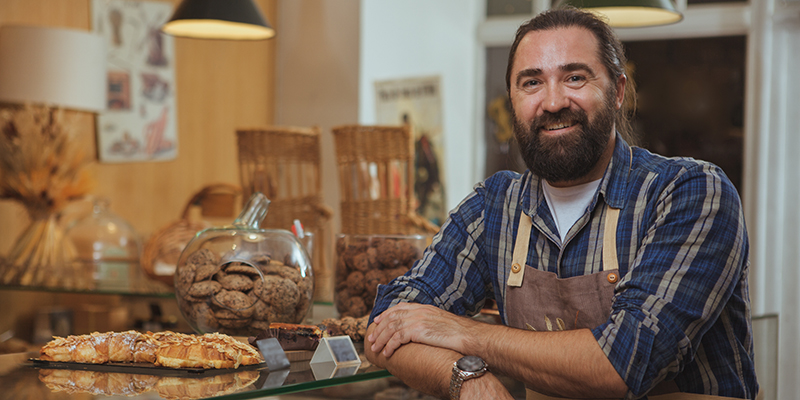 Handsome mature bearded male baker smiling to the camera proudly, working at his bakery shop