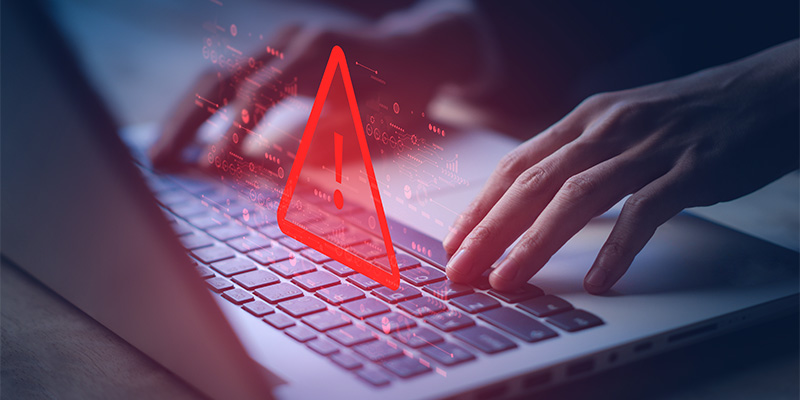 Person typing on laptop with warning sign floating above keyboard