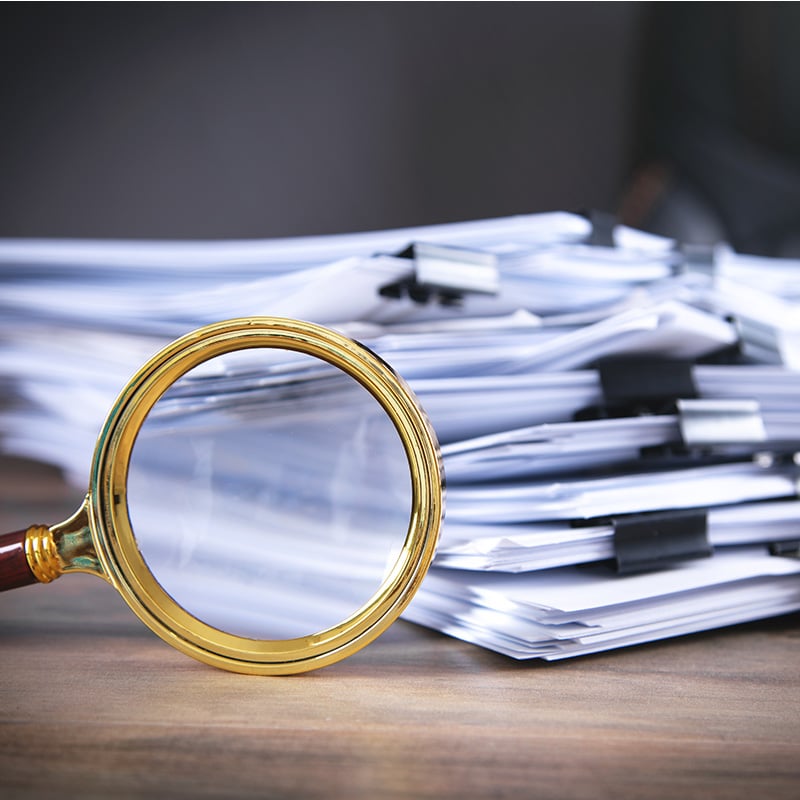 Stack of clipped documents with a magnifying glass in front of stack