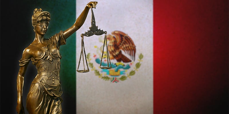 Bronze statue holding scales in front of the Mexican flag