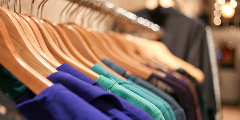 Several cool colored shirts hang on wooden hangers across a rack.