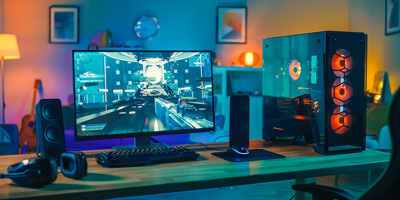 Powerful Personal Computer Gamer Rig with First-Person Shooter Game on Screen. Monitor Stands on the Table at Home. Cozy Room with Modern Design is Lit with Warm and Neon Light.